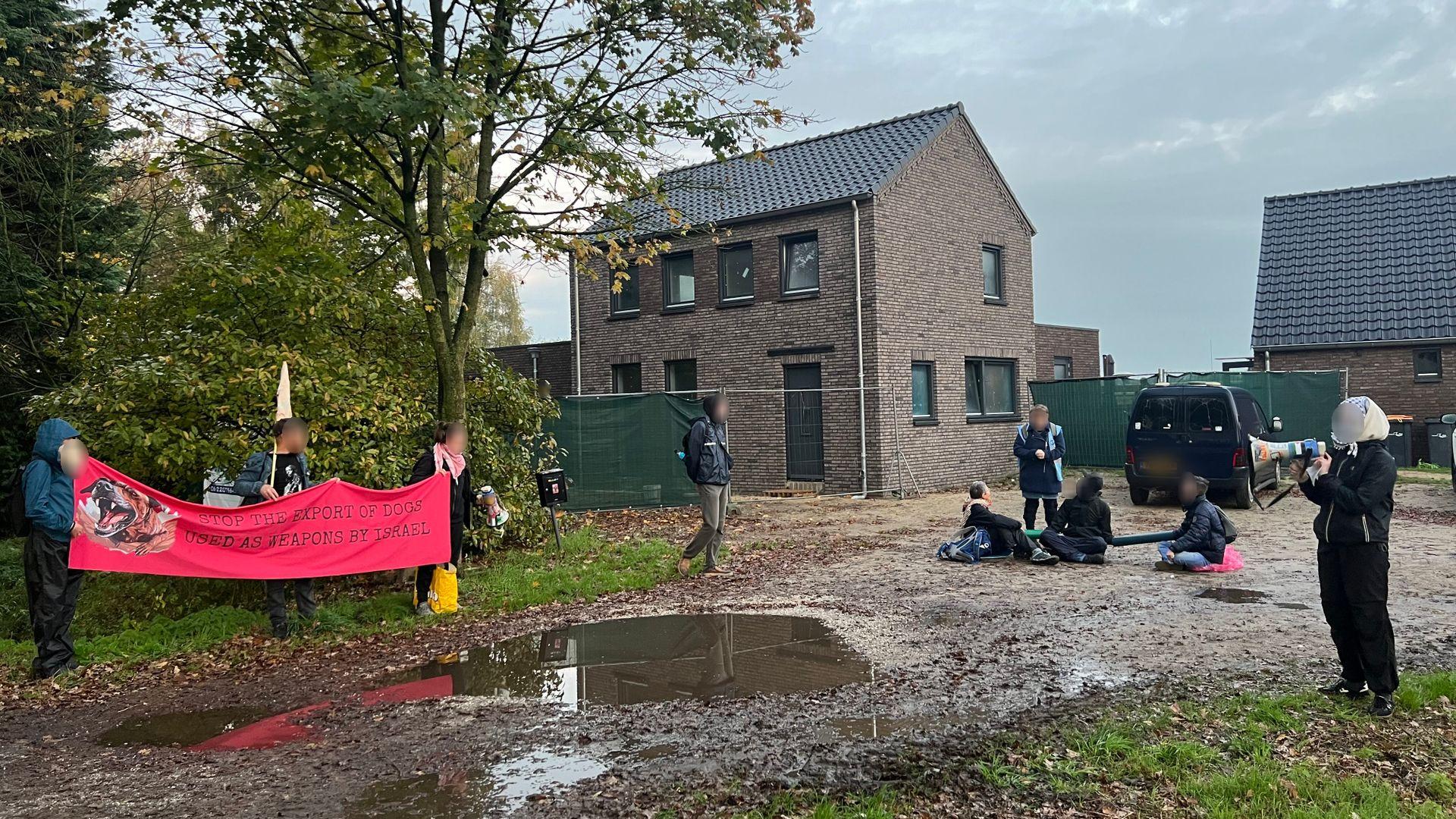 Een groep demonstranten op een modderig terrein. Enkelen van hen zitten op de grond met hun armen in een lock-on. Anderen houden een spandoek op. 